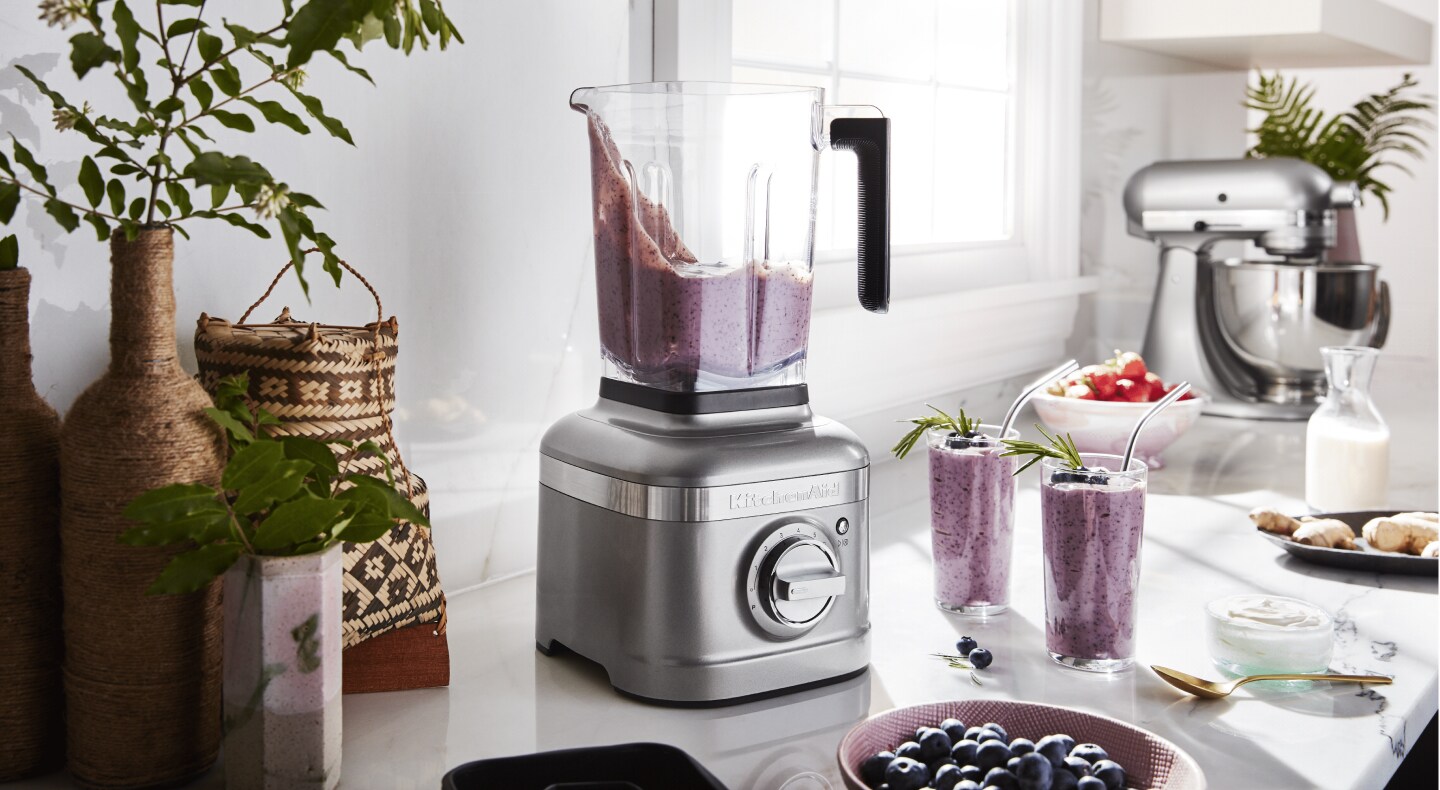 Silver KitchenAid® blender with smoothie next to two glasses of smoothie Silver KitchenAid® blender with smoothie next to two glasses of smoothie